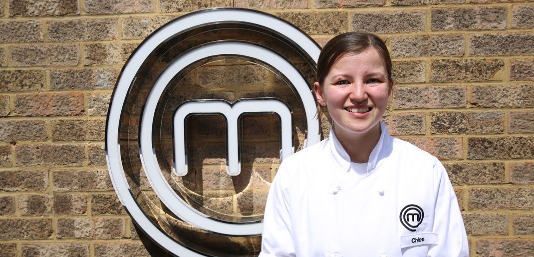 Young lady in white chefs apron in front of MasterChef logo