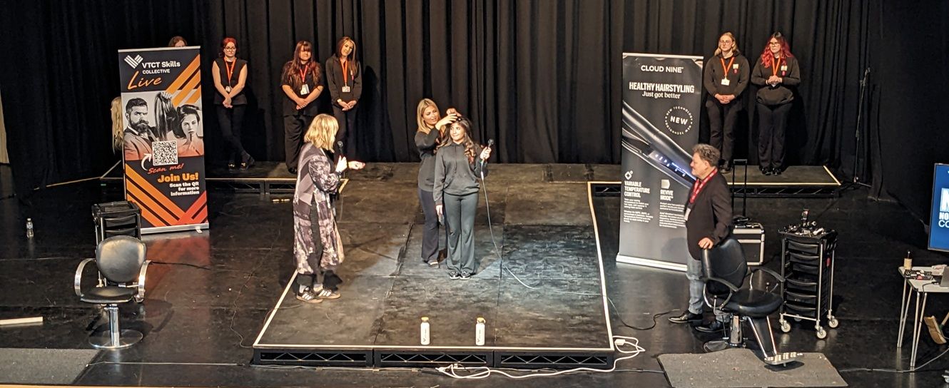 Hairdressing students on stage with two presenters either side