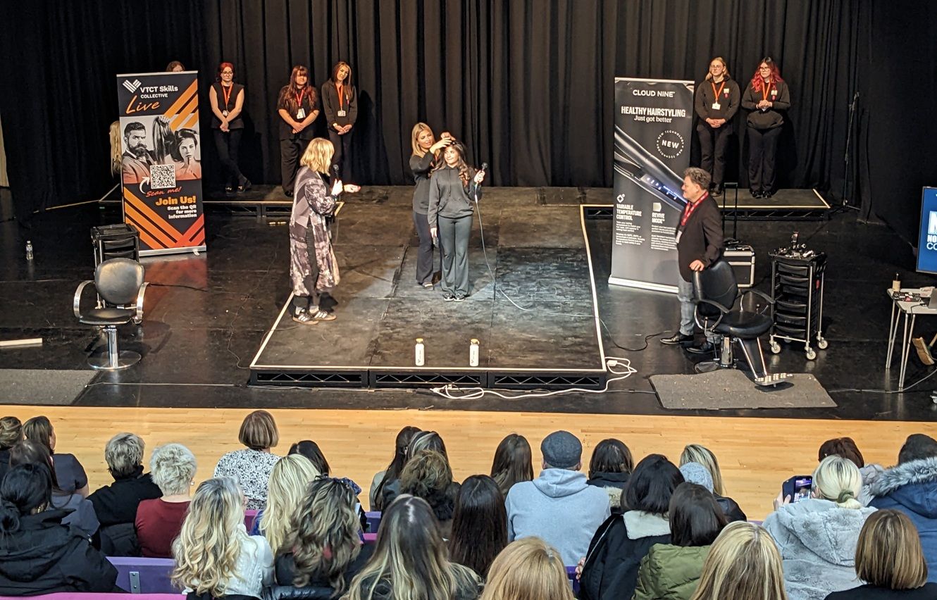 Hairdressing students on stage with two presenters either side